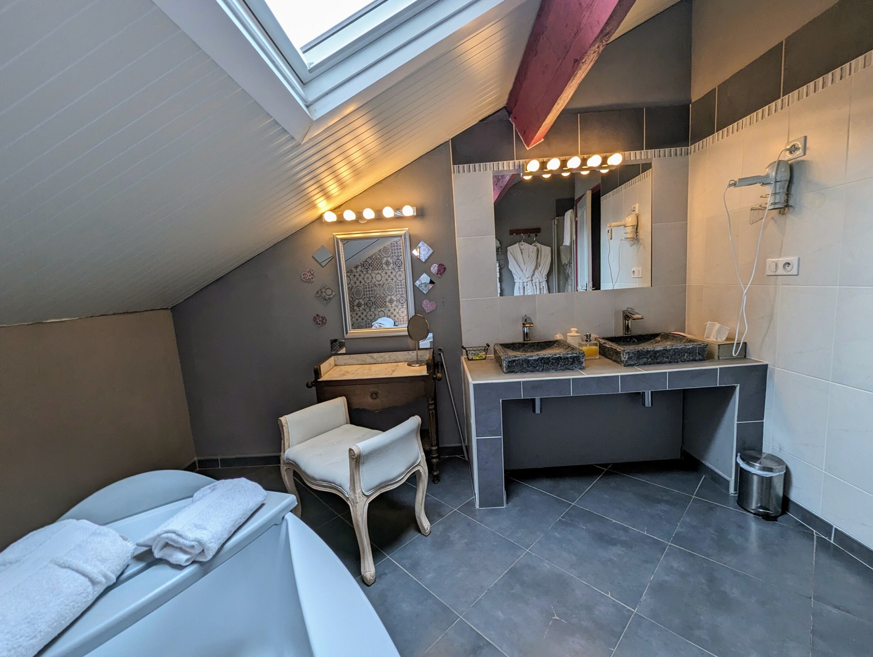 A modern bathroom with a skylight, a vanity with two sinks, a mirror, and a chair.