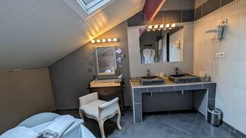 A modern bathroom with a skylight, a vanity with two sinks, a mirror, and a chair.