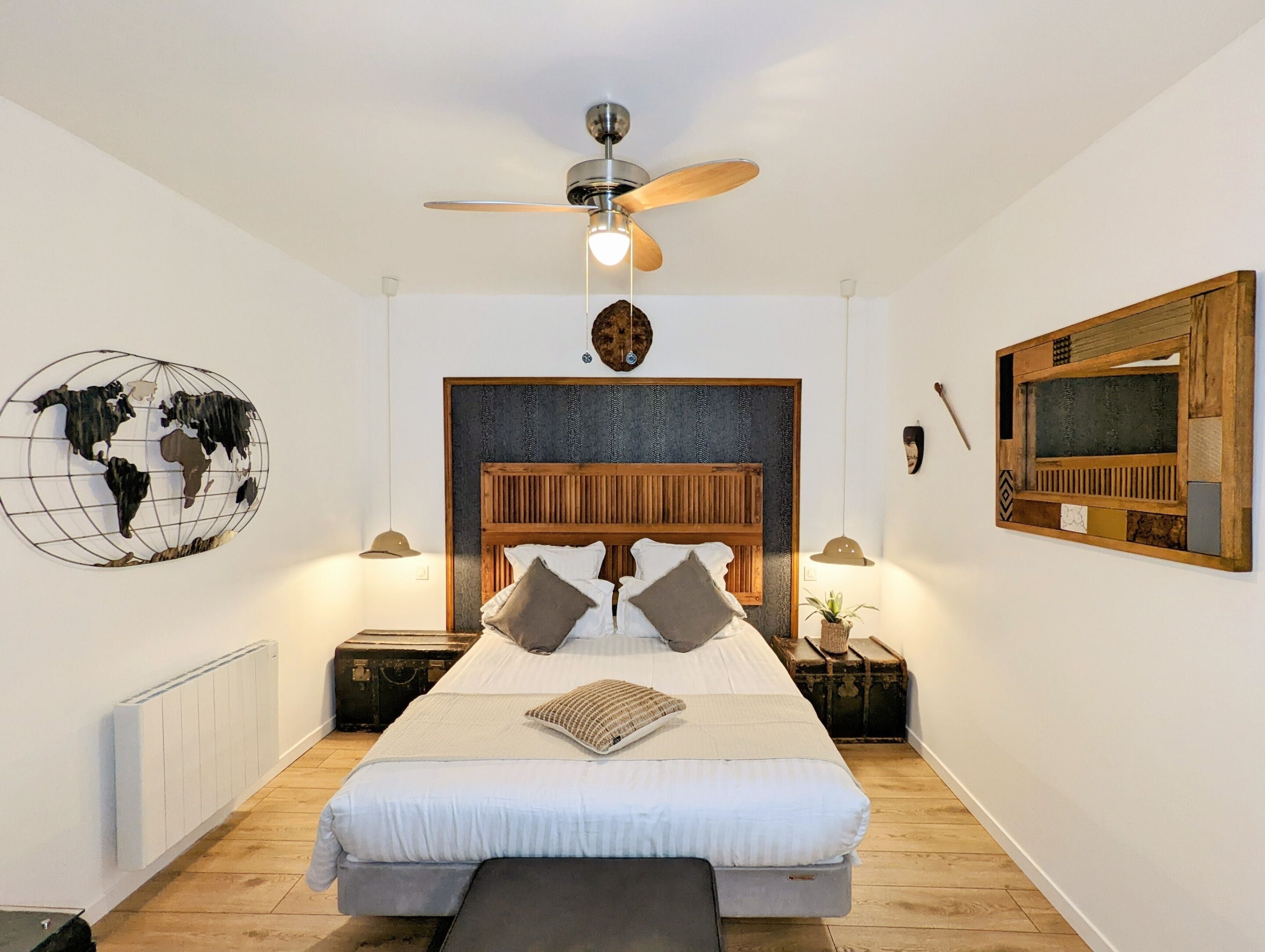 A bedroom with a large bed, a wooden headboard, a globe wall art, a ceiling fan, and a world map on the wall.