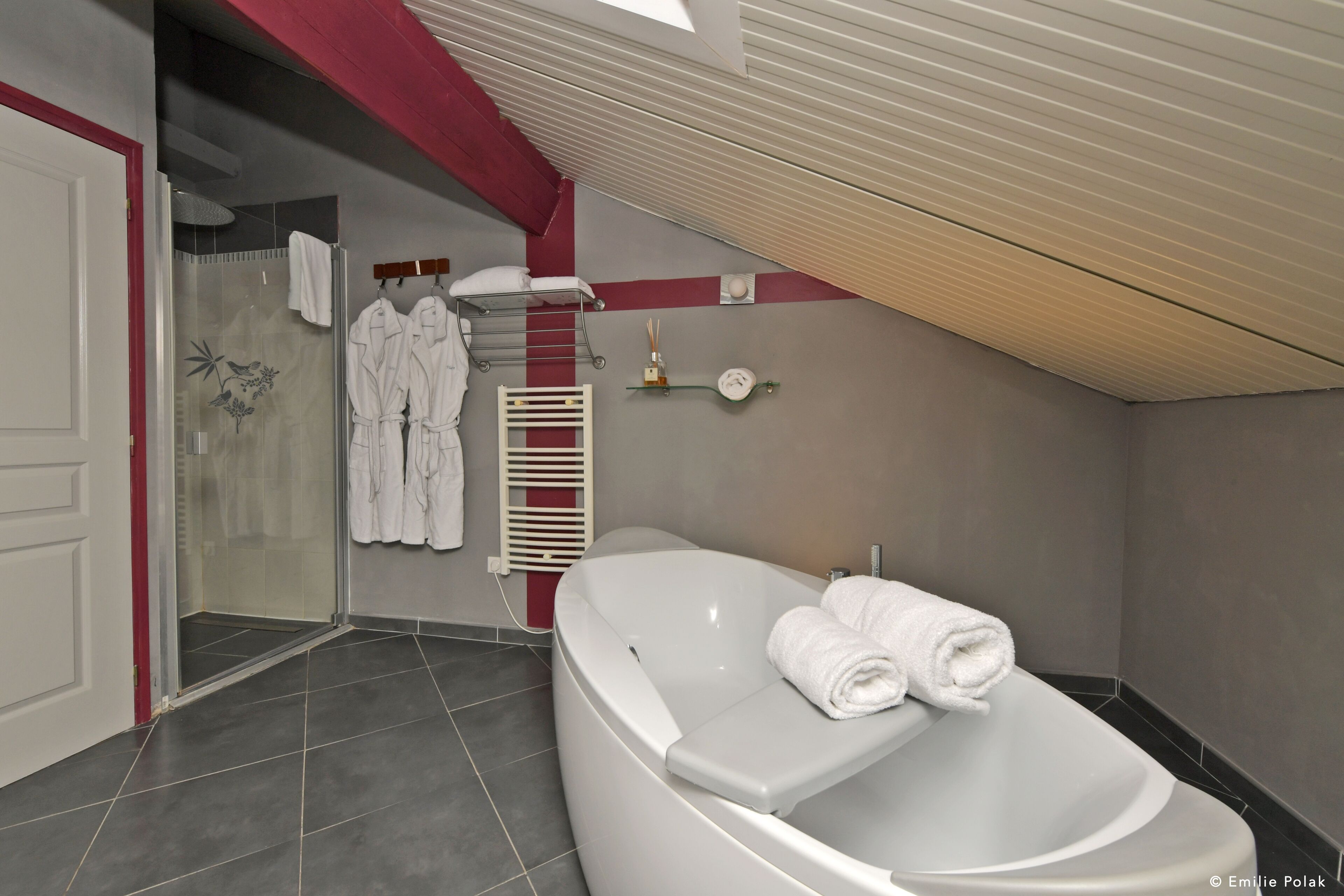 Une salle de bain moderne avec une baignoire sur pieds, une douche en verre et un porte-serviettes avec deux peignoirs blancs.