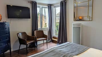 Un dormitorio con cama, dos sillas, cómoda, televisor, ventana con cortinas y radiador.