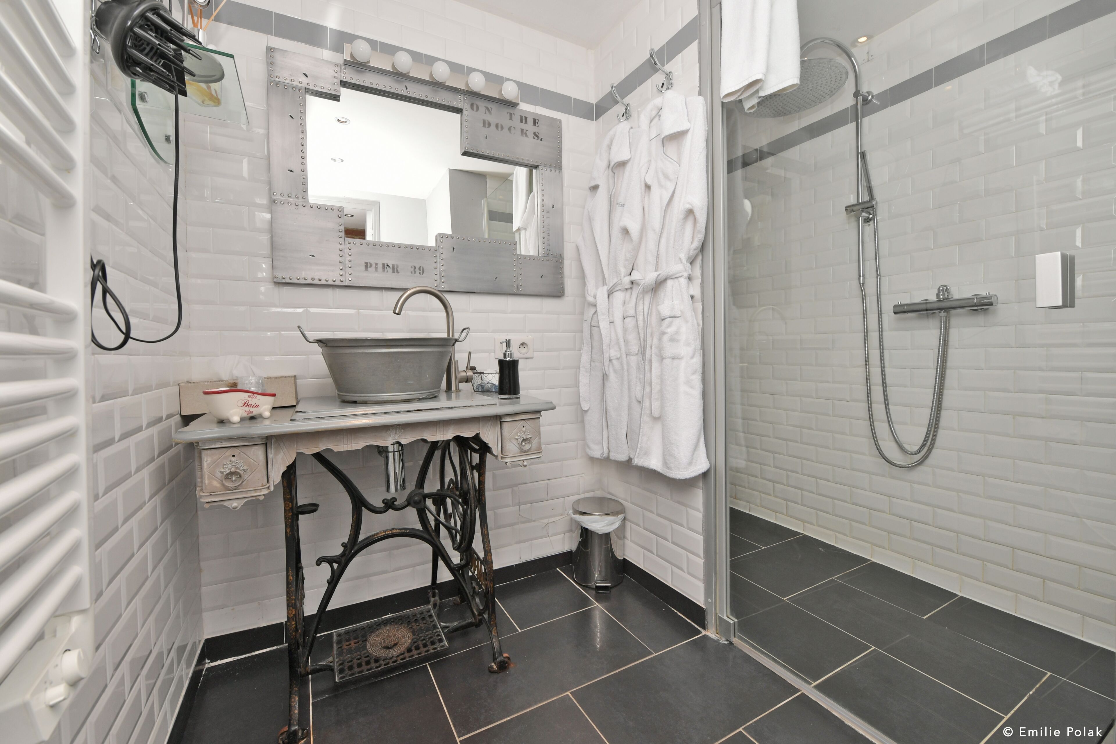 Een badkamer met een vintage wastafel, een spiegel met verlichting, een douche en een handdoekhouder.