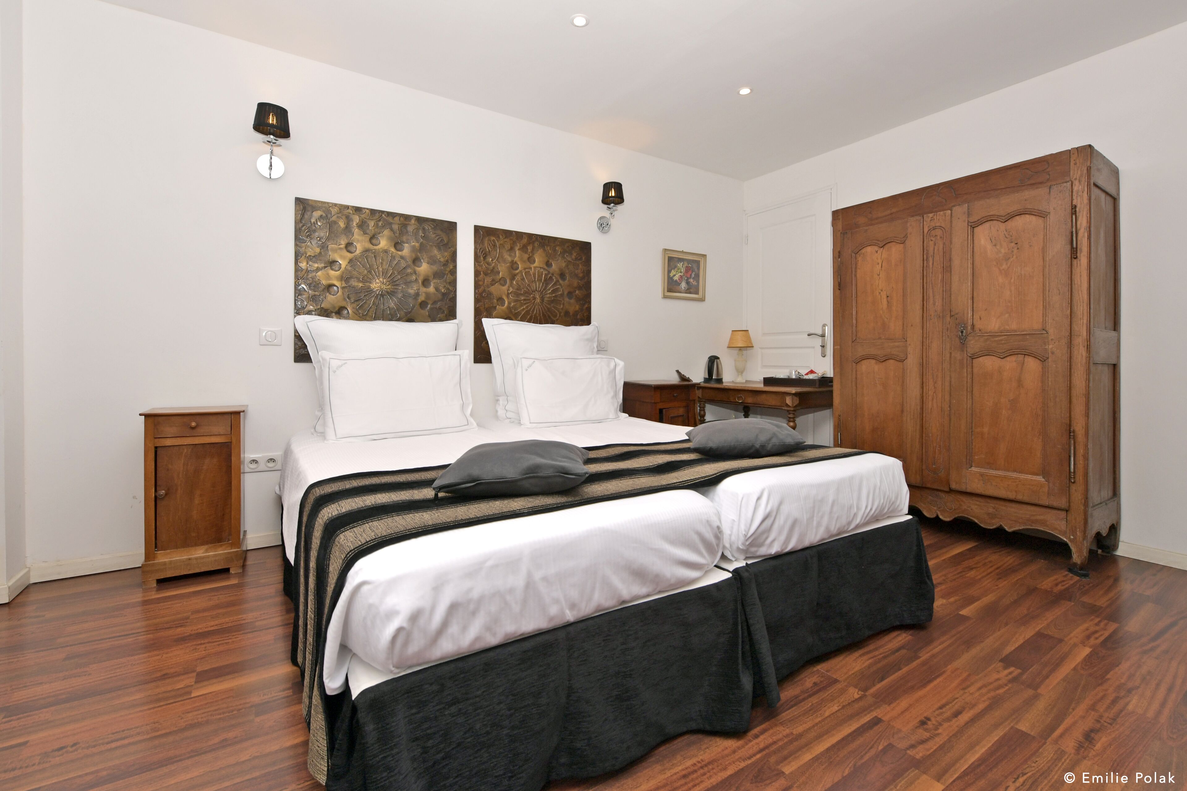 Une chambre avec un grand lit, une armoire en bois et deux appliques murales.