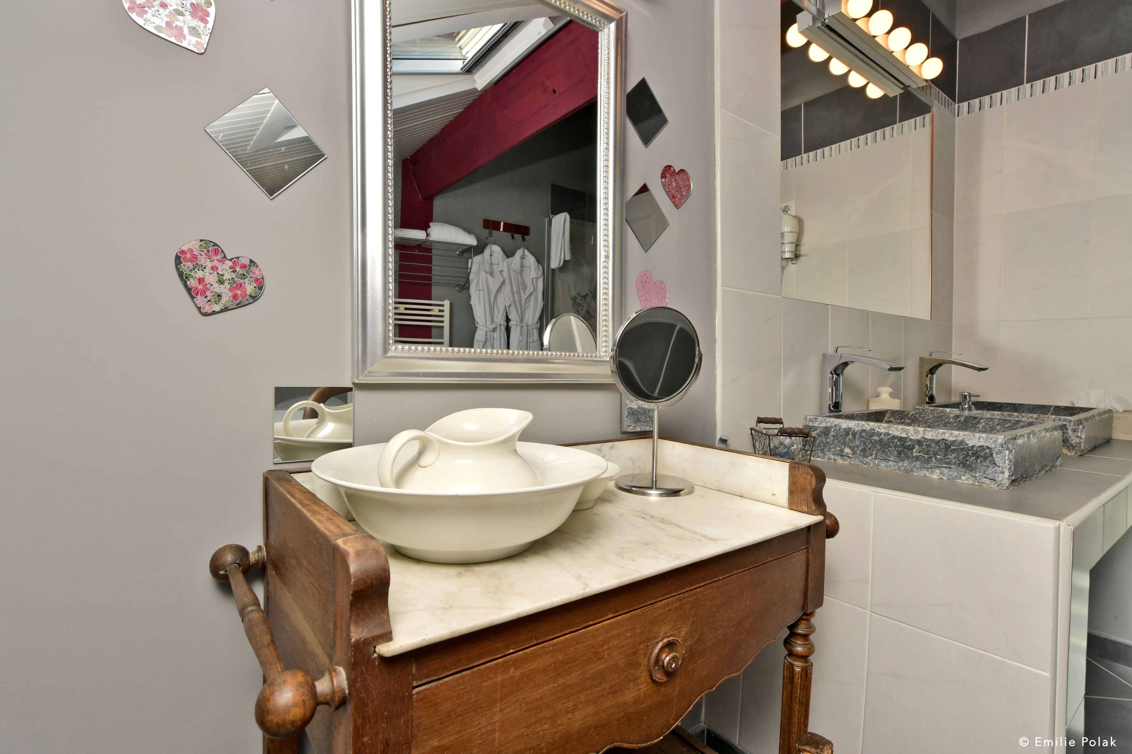 Un baño con tocador de madera, un espejo grande, un lavabo con encimera de mármol y elementos decorativos con forma de corazón en la pared.