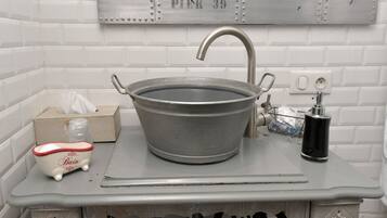 A bathroom with a large metal basin sink, a small decorative bathtub, and a towel rack.