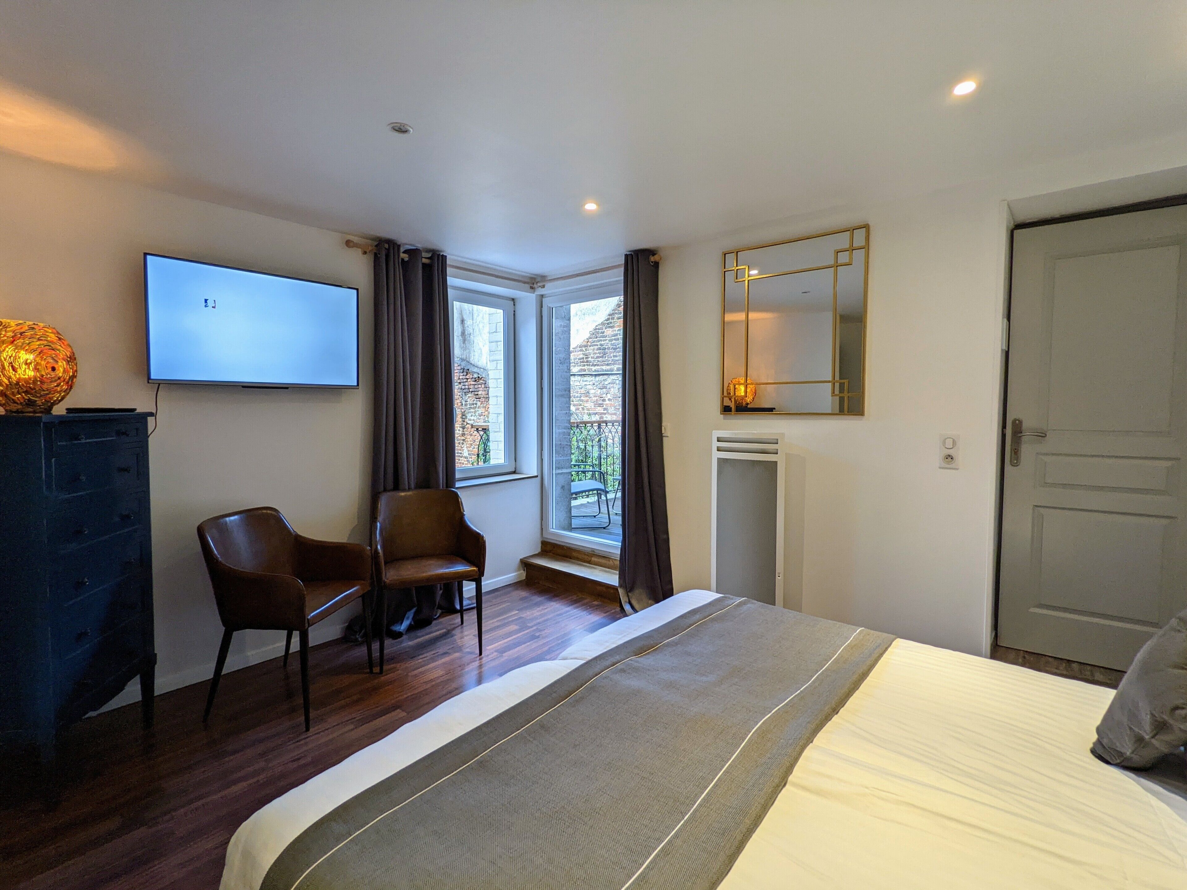 A hotel room with a bed, a TV, a chair, a fireplace, a window with curtains, and a door.
