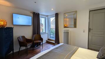 A hotel room with a bed, a TV, a chair, a fireplace, a window with curtains, and a door.