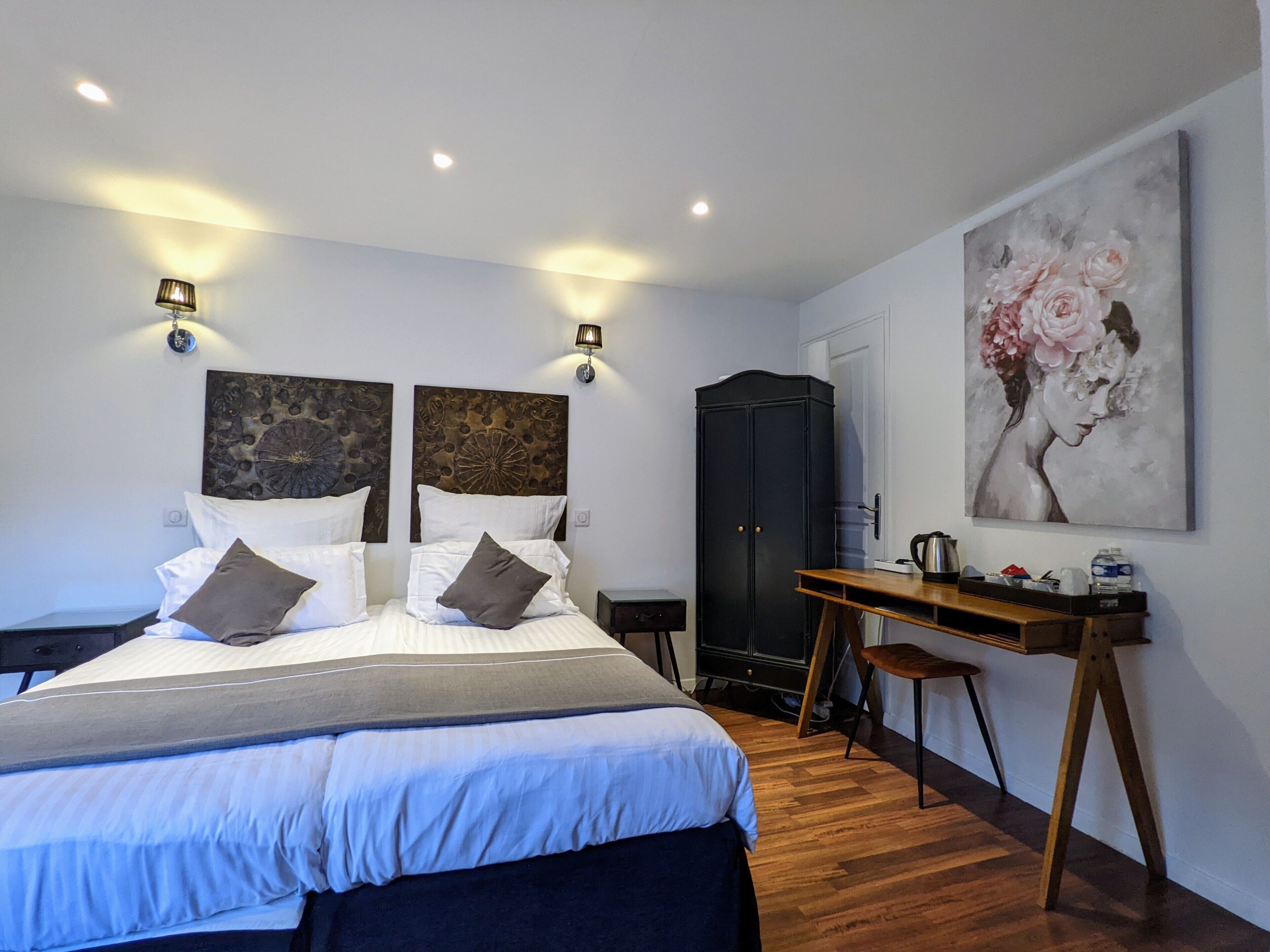 A bedroom with a bed, bedside tables, a desk, a wardrobe, and a painting on the wall.