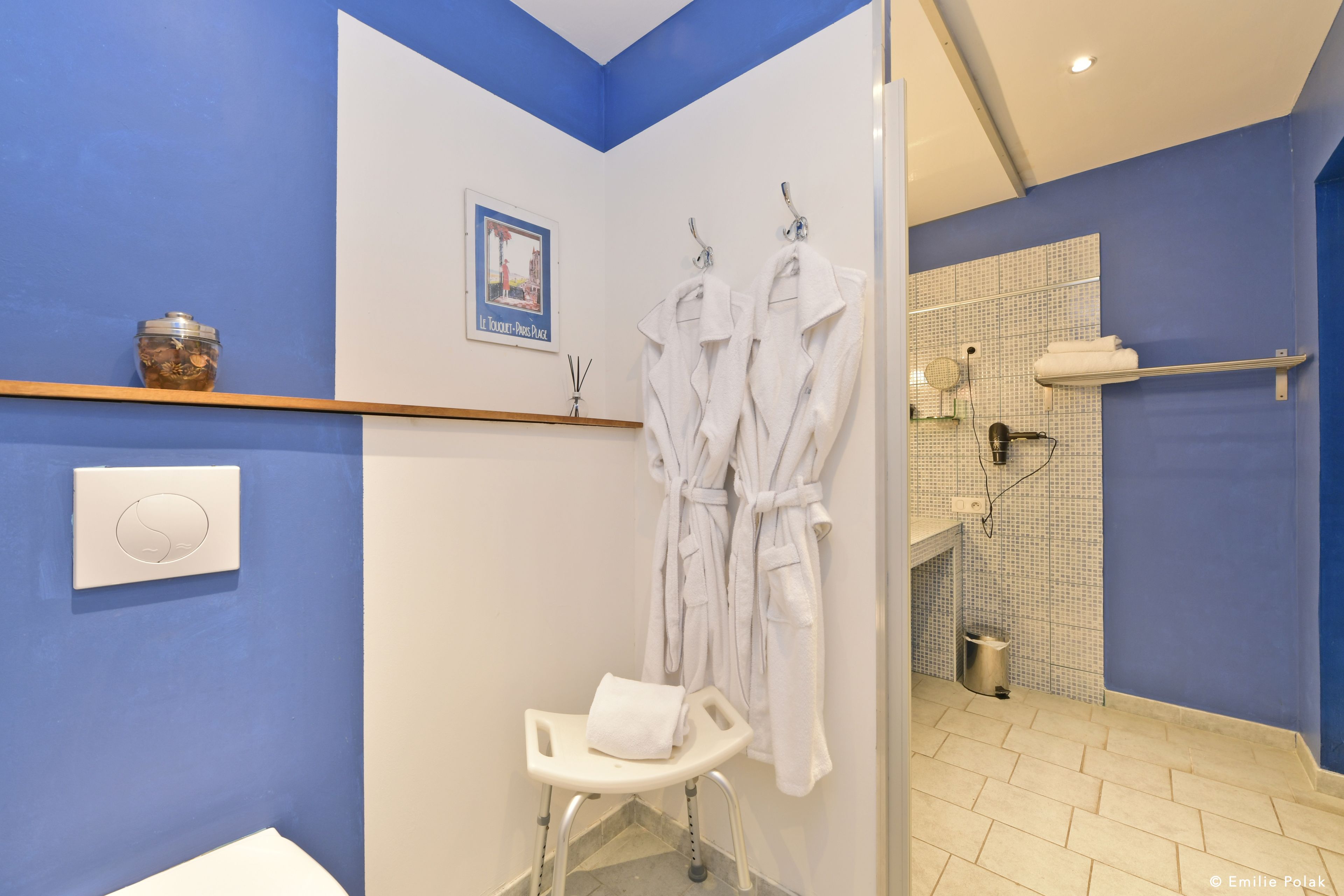 Un baño con paredes azules, un inodoro blanco, una zona de ducha y dos toallas blancas colgadas en ganchos.