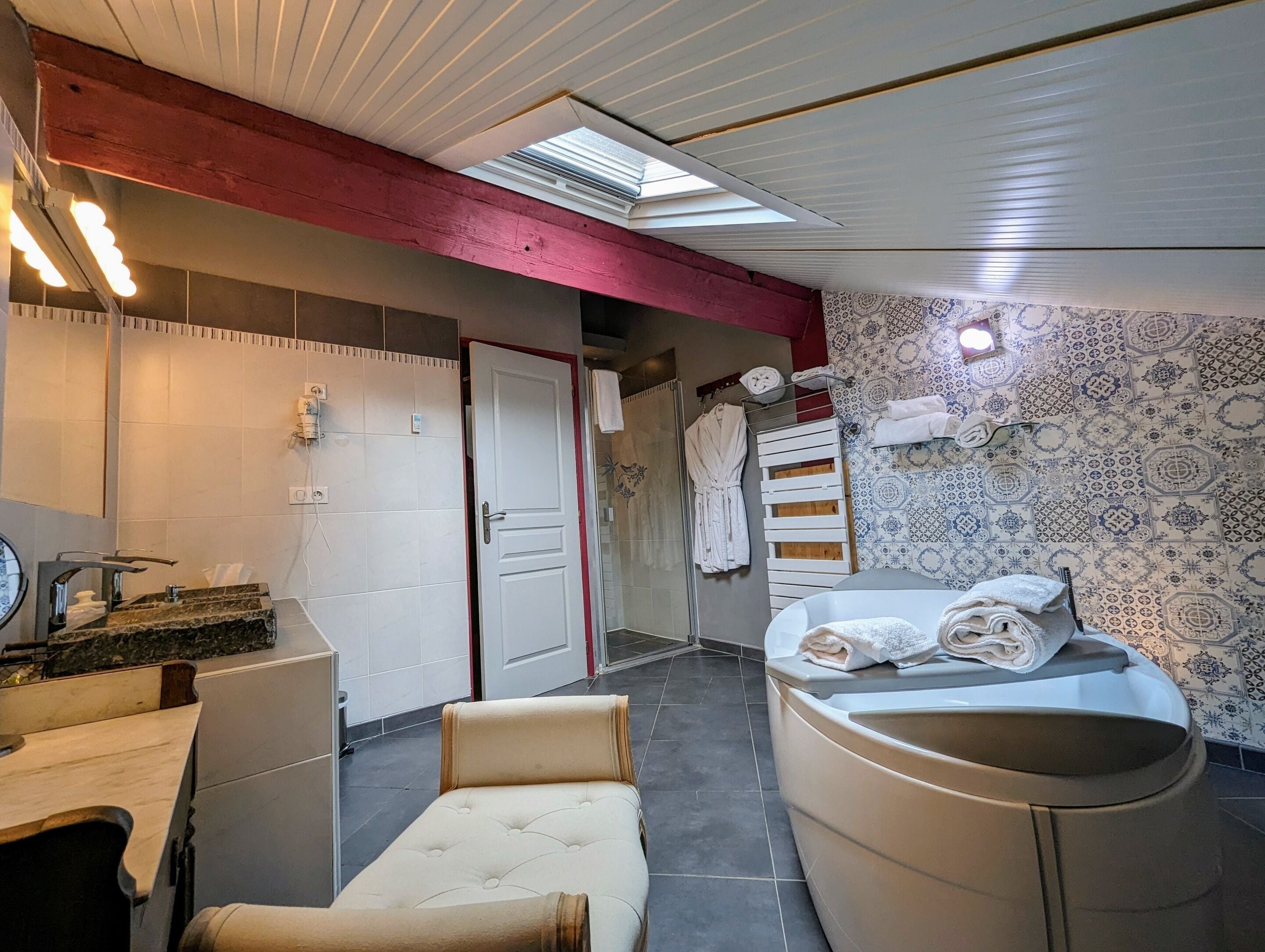 A bathroom with a bathtub, a shower, and a toilet. There is a towel rack with towels and a robe hanging on it. The walls have a patterned tile design.