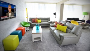 A modern living room with a grey sofa, colorful ottomans, a green chair, and a coffee table with a blue vase. - 3 Lakes Hostel (Killarney)
