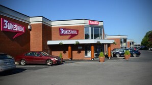 A 3 Lakes Hostel building with a red and white sign, a parking lot with cars, and potted plants in front. - 3 Lakes Hostel (Killarney)