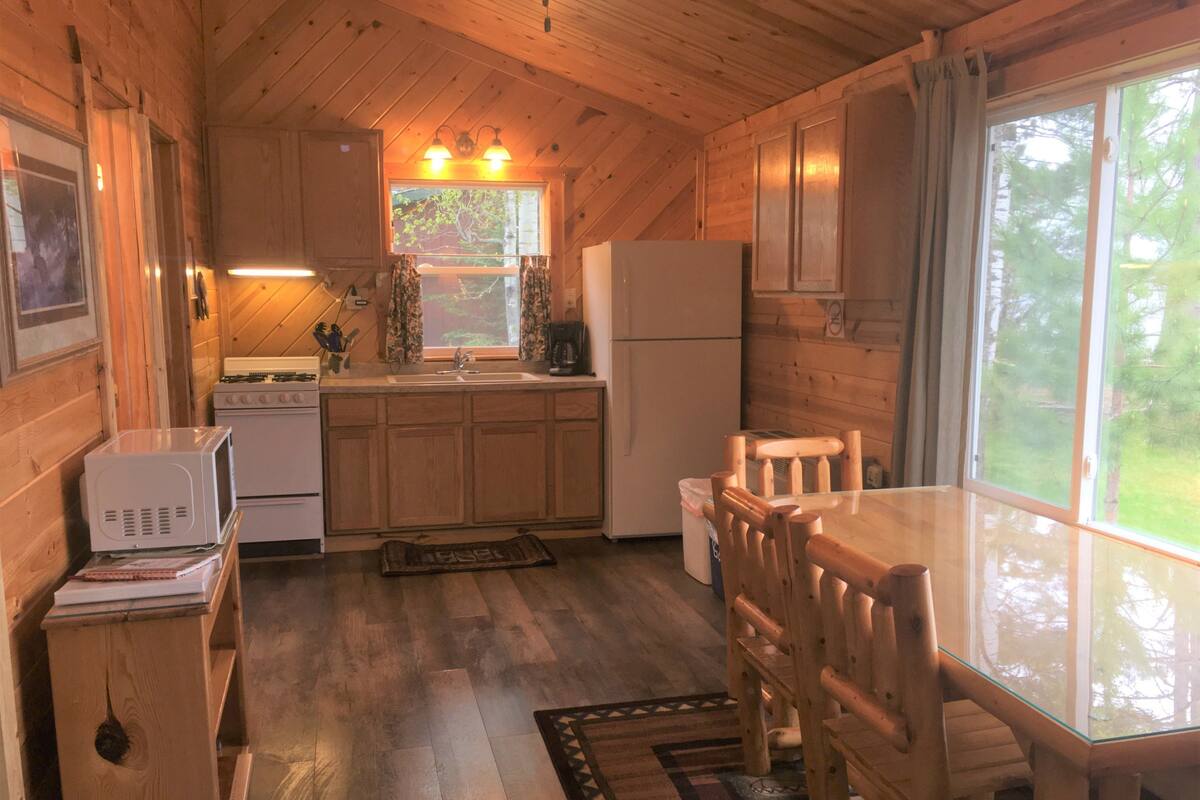 A wooden cabin kitchen with a refrigerator, stove, microwave, and wooden dining table.