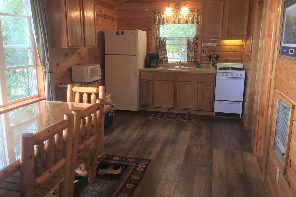 A wooden cabin kitchen with a refrigerator, stove, microwave, and wooden cabinets.