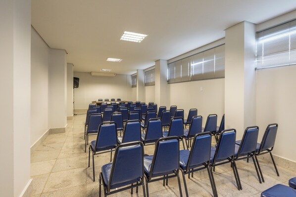 A conference room with rows of blue chairs, a tiled floor, and a white ceiling with recessed lighting.