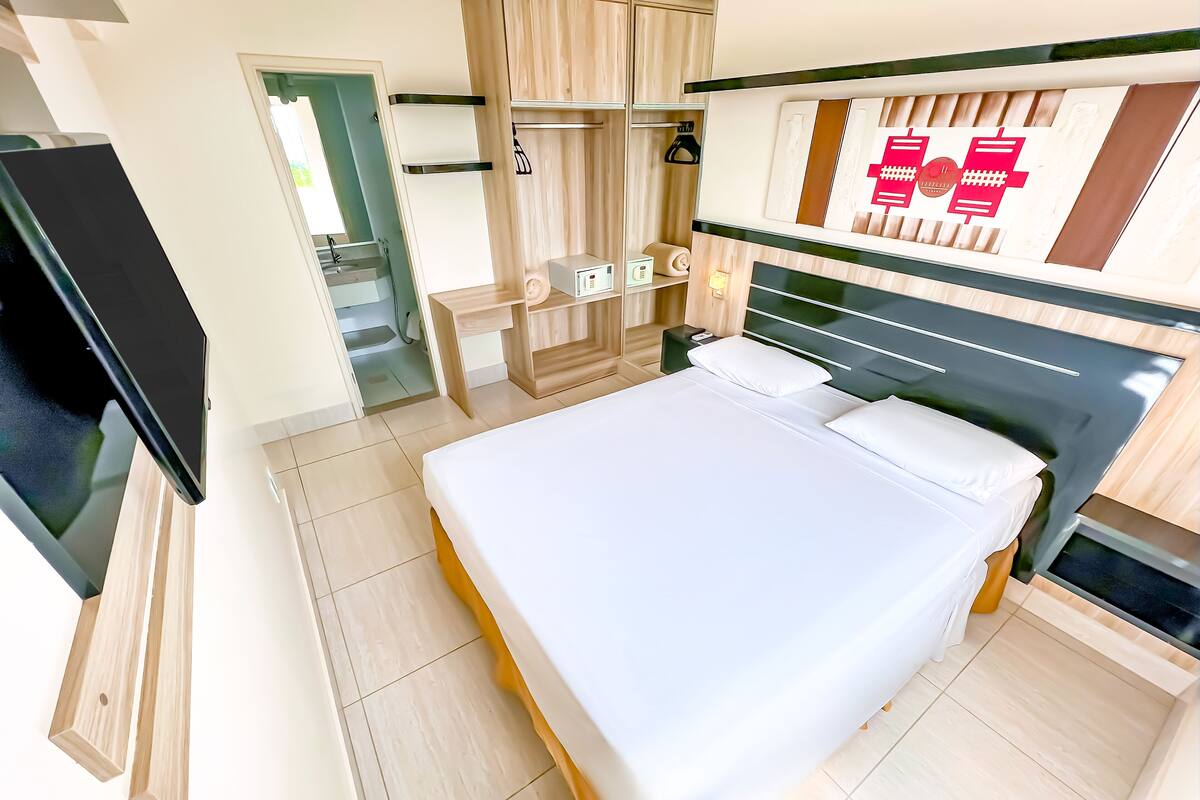 Ein modernes Hotelzimmer mit einem großen Bett, einem Flachbildfernseher, einem Kleiderschrank und einem Schminktisch mit Spiegel.