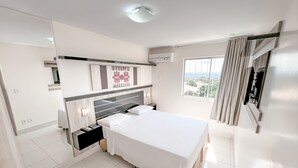 A modern bedroom with a large bed, a nightstand, a wall-mounted TV, and a window with curtains.