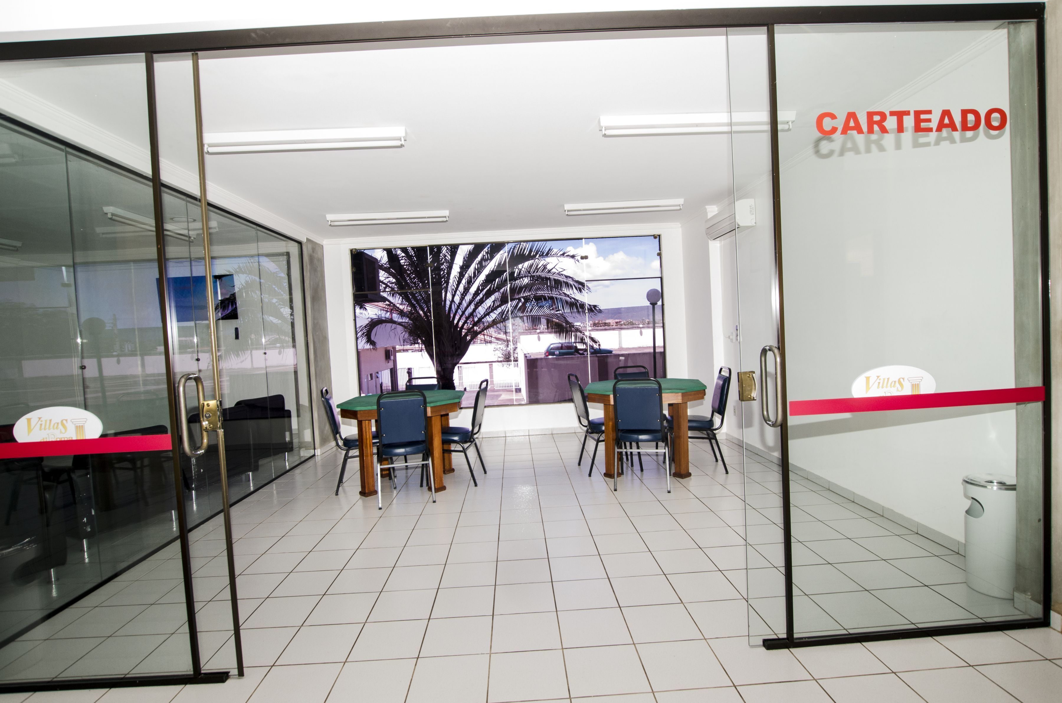 A reception area with glass doors, a reception desk, and a view of palm trees outside.