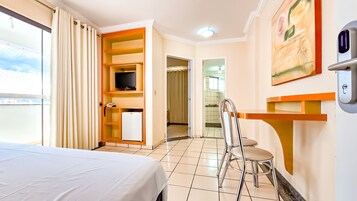 A hotel room with a bed, a TV, a desk, and a chair. There is a bathroom visible through an open door.