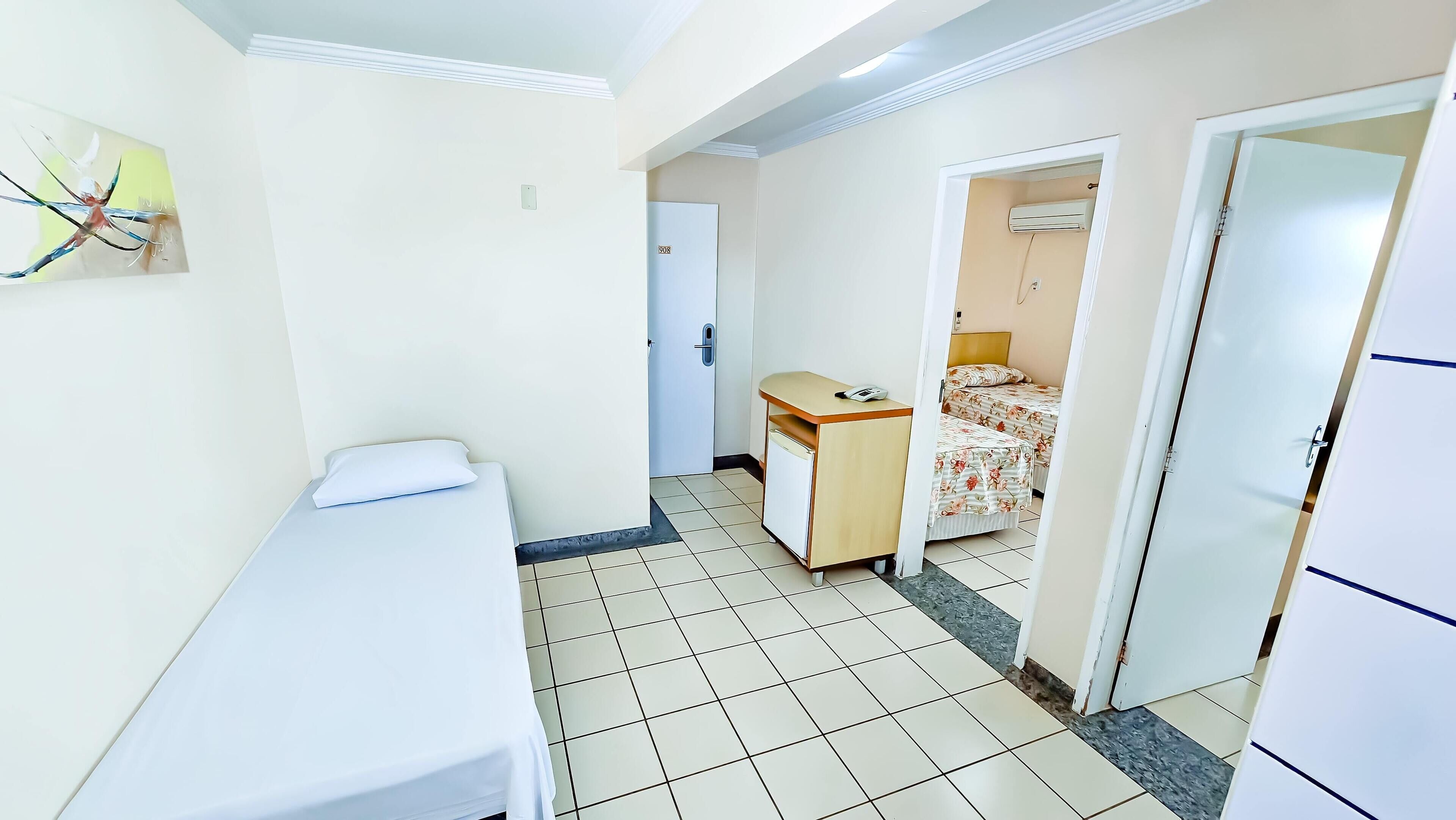 A small, clean room with a bed, a desk, and a door leading to another room.