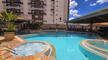A swimming pool with a hot tub, lounge chairs, and a building in the background.