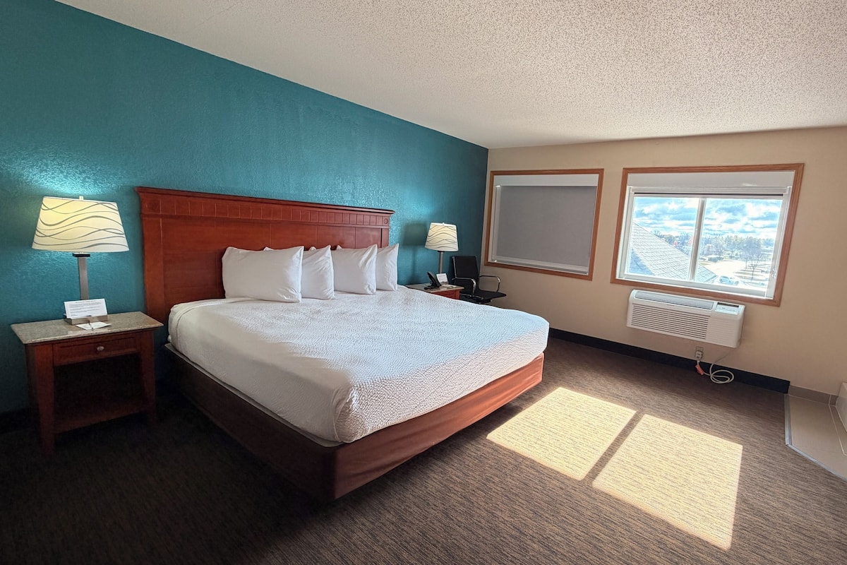 Une chambre d’hôtel avec un grand lit, deux tables de chevet avec des lampes, une fenêtre donnant sur un beau paysage et une salle de bain avec une baignoire et un porte-serviettes.