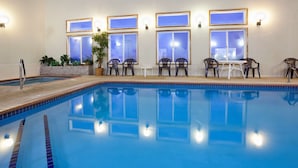 An indoor swimming pool with clear water, surrounded by chairs and tables, and illuminated windows.
