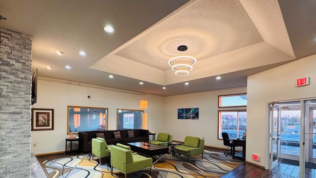 A lobby with a modern design, featuring a patterned carpet, a seating area with green chairs, a black sofa, and a wooden reception desk.