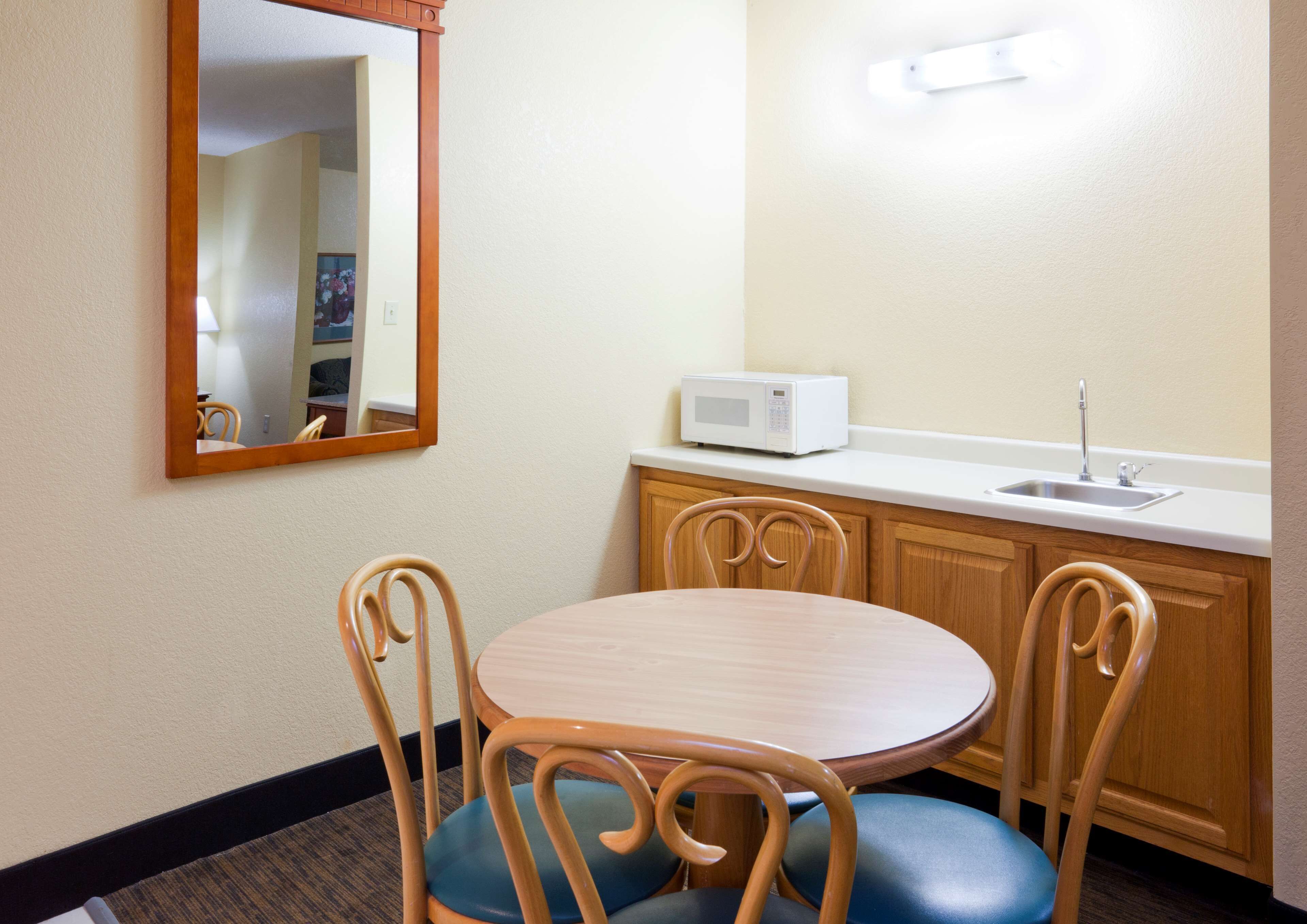 A compact kitchenette with a microwave, sink, and wooden cabinets.