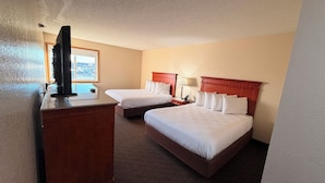 A hotel room with two beds, a TV on a wooden dresser, and a window with a view of parked cars.