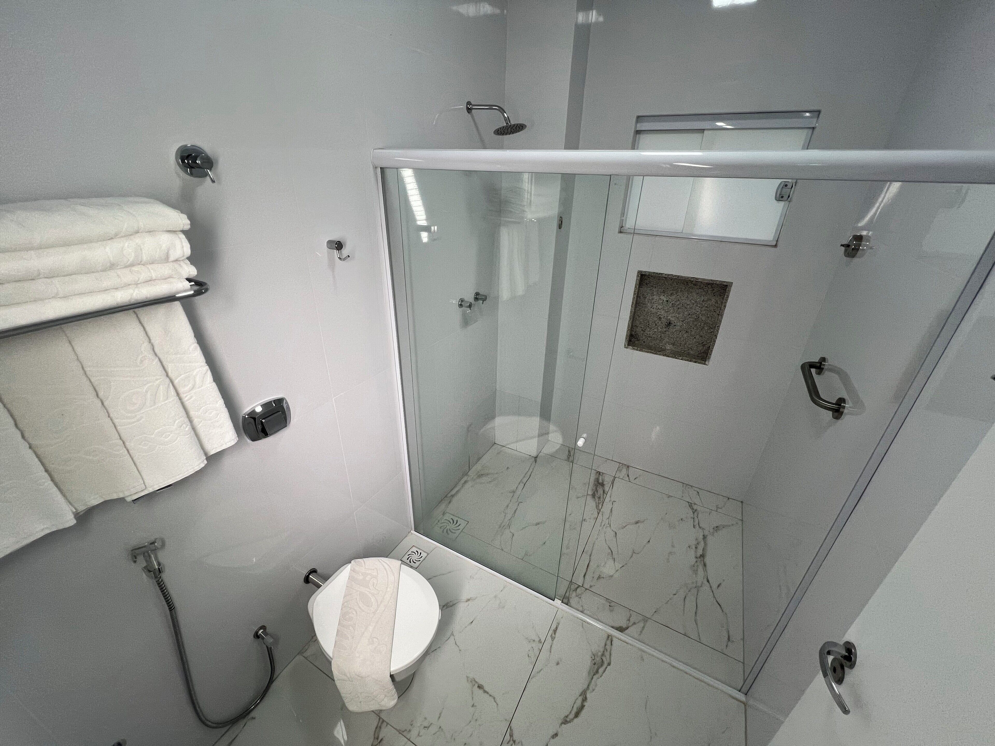 A bathroom with a glass-enclosed shower, a toilet, and a towel rack with folded towels.