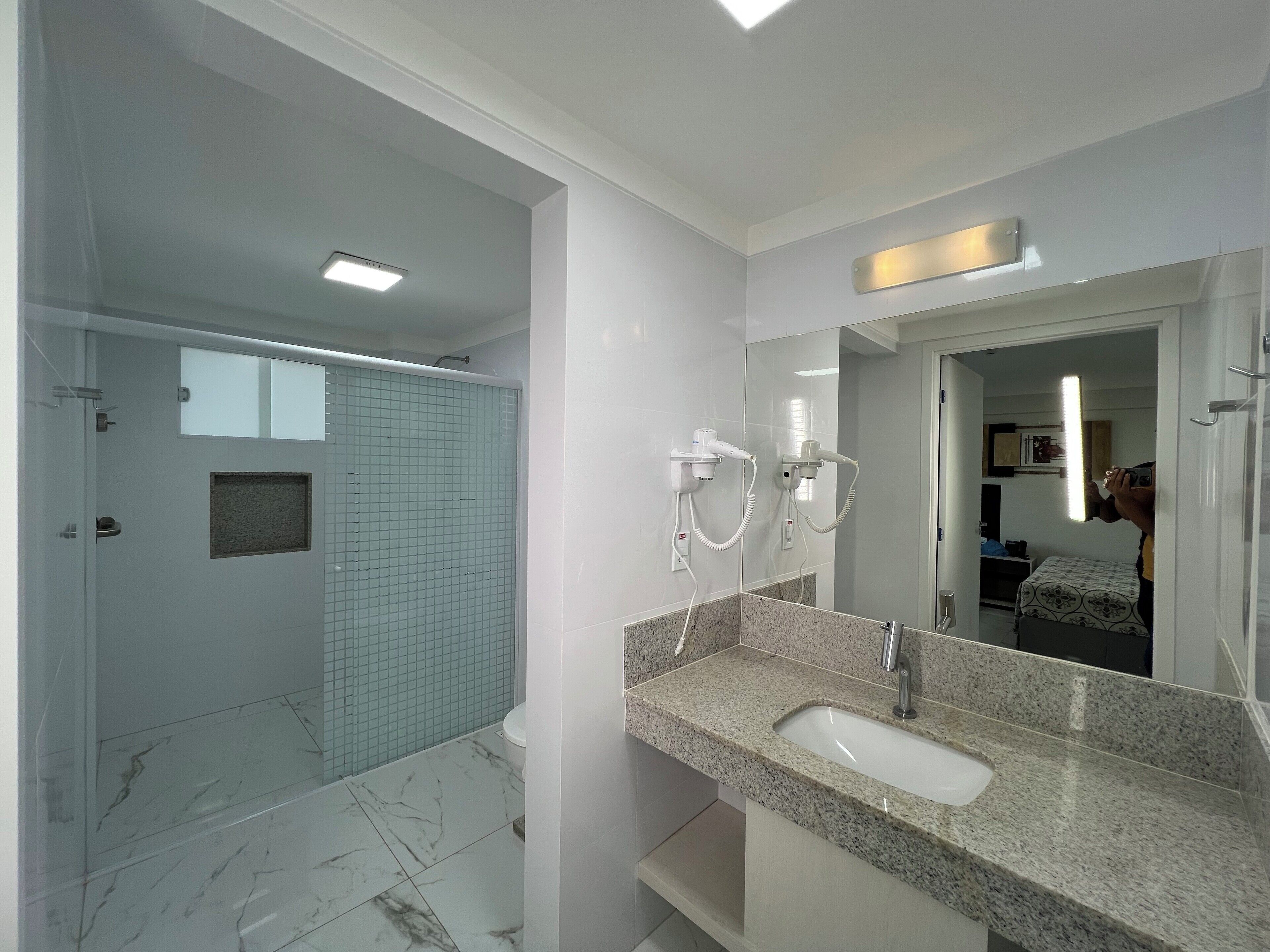 Une salle de bain moderne avec un lavabo en marbre, une cabine de douche en verre et un grand miroir.