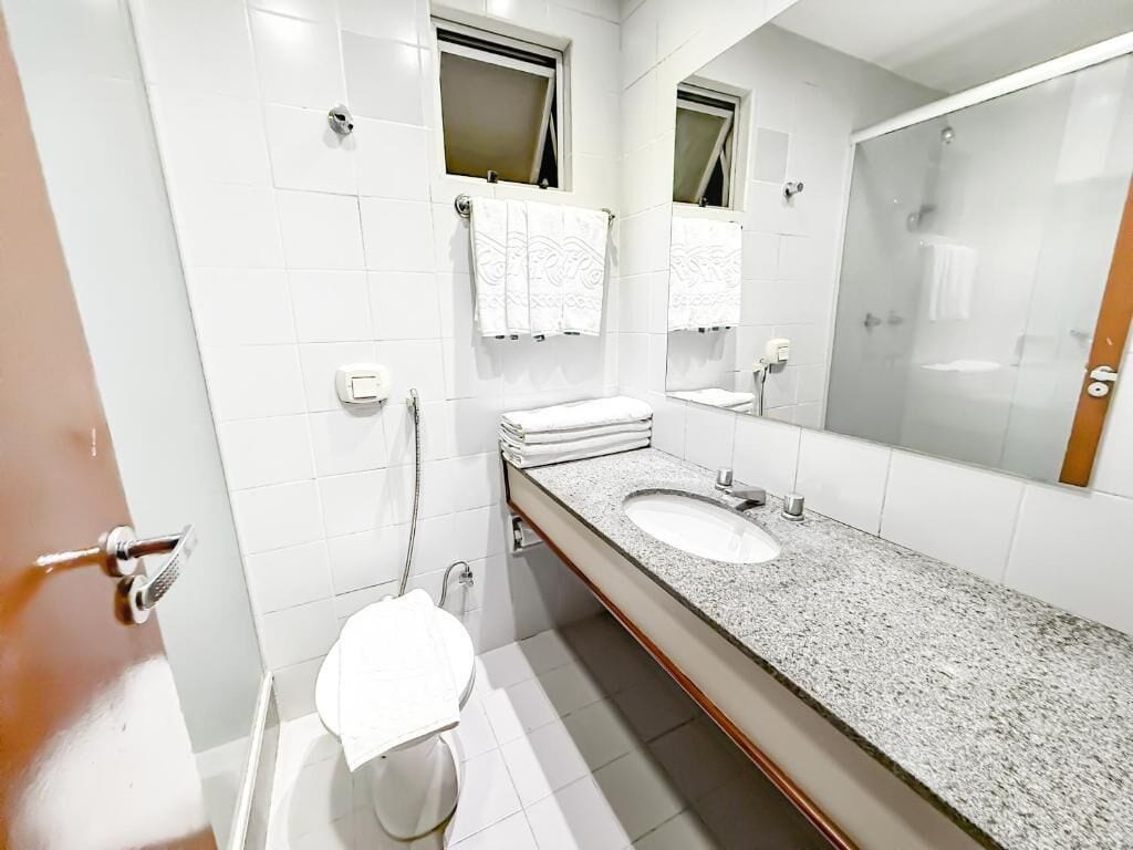 Un baño moderno con un lavamanos grande, dos percheros para toallas, un inodoro y un espejo.