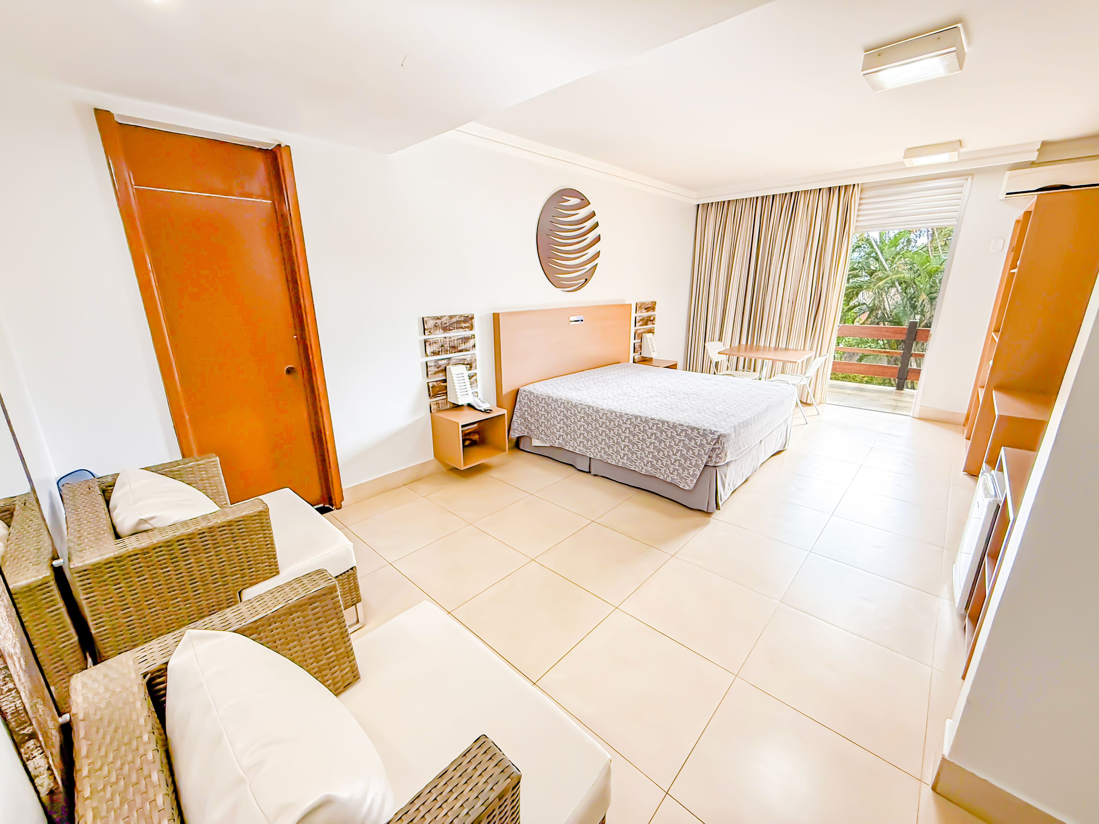 Une chambre d’hôtel avec un lit, une petite table, une chaise, un canapé en osier et une vue sur l’extérieur.