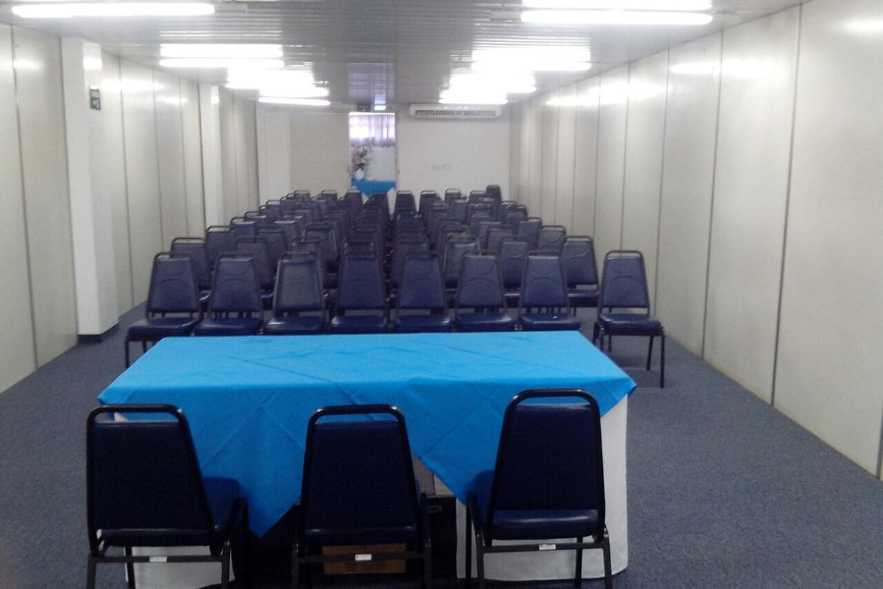 Un salón de conferencias con filas de sillas y una mesa cubierta con mantel azul.