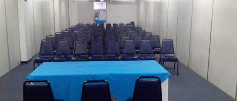 Un salón de conferencias con filas de sillas y una mesa cubierta con mantel azul.