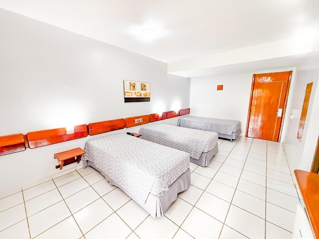 Habitación de hotel con tres camas, una mesita, un banco y una puerta.