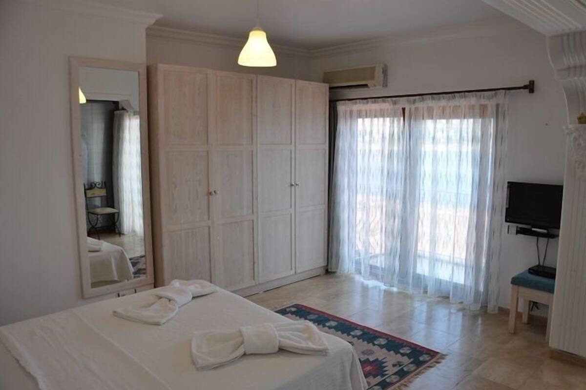 Una habitación de hotel con cama, un armario grande, televisor y ventana con cortinas.