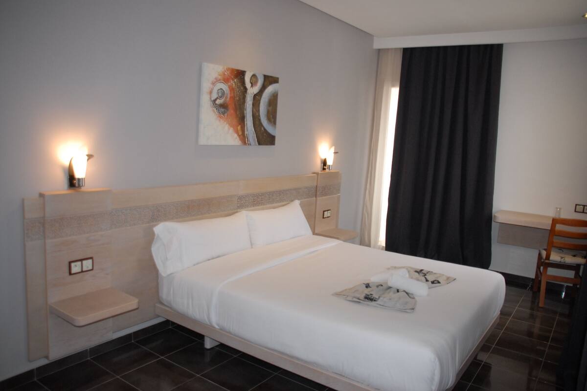 A hotel room with a large bed, bedside tables, a desk, and a chair.