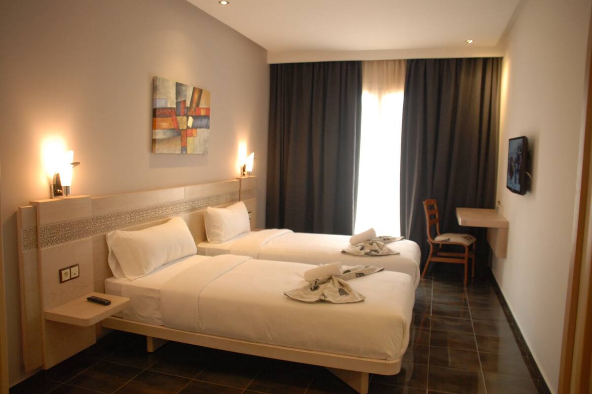 A hotel room with two beds, a desk, and a chair.
