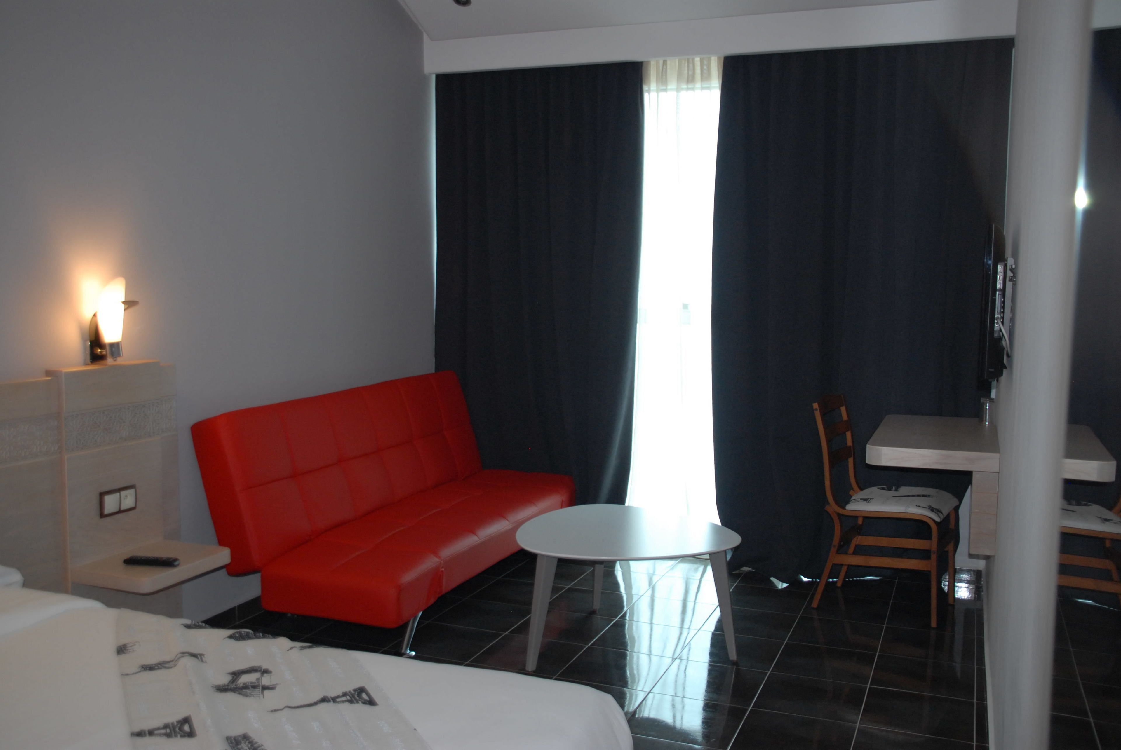 Habitación de hotel con un sofá rojo, una pequeña mesa redonda, una silla de madera, una cama y un televisor.