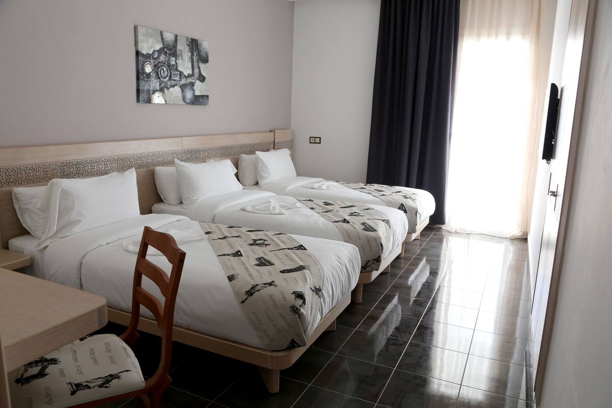 A hotel room with three beds, a wooden headboard, a desk, and a chair.