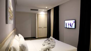 A hotel room with a bed, a television mounted on the wall, and a wardrobe.