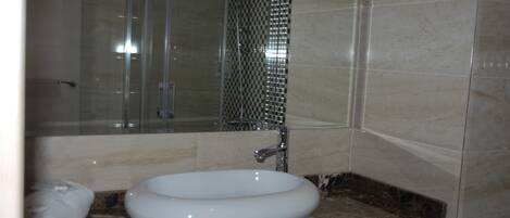 Un baño con lavamanos blanco, cabina de ducha de vidrio y encimeras de mármol.