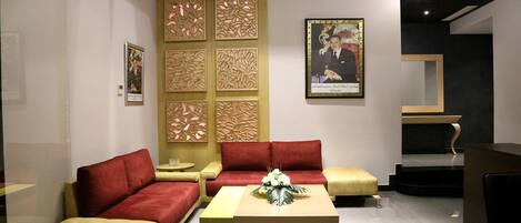 Un área de espera moderna con un sofá rojo, un reposapiés color beige y una mesa de centro de madera con un centro de mesa floral.