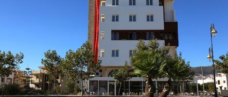 Un hotel de diseño moderno, con llamante franja vertical roja en la fachada, varios balcones y un área de entrada de vidrio.