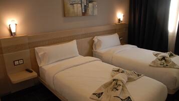 Habitación de hotel con dos camas, una mesita de noche con control remoto y lámparas de pared.