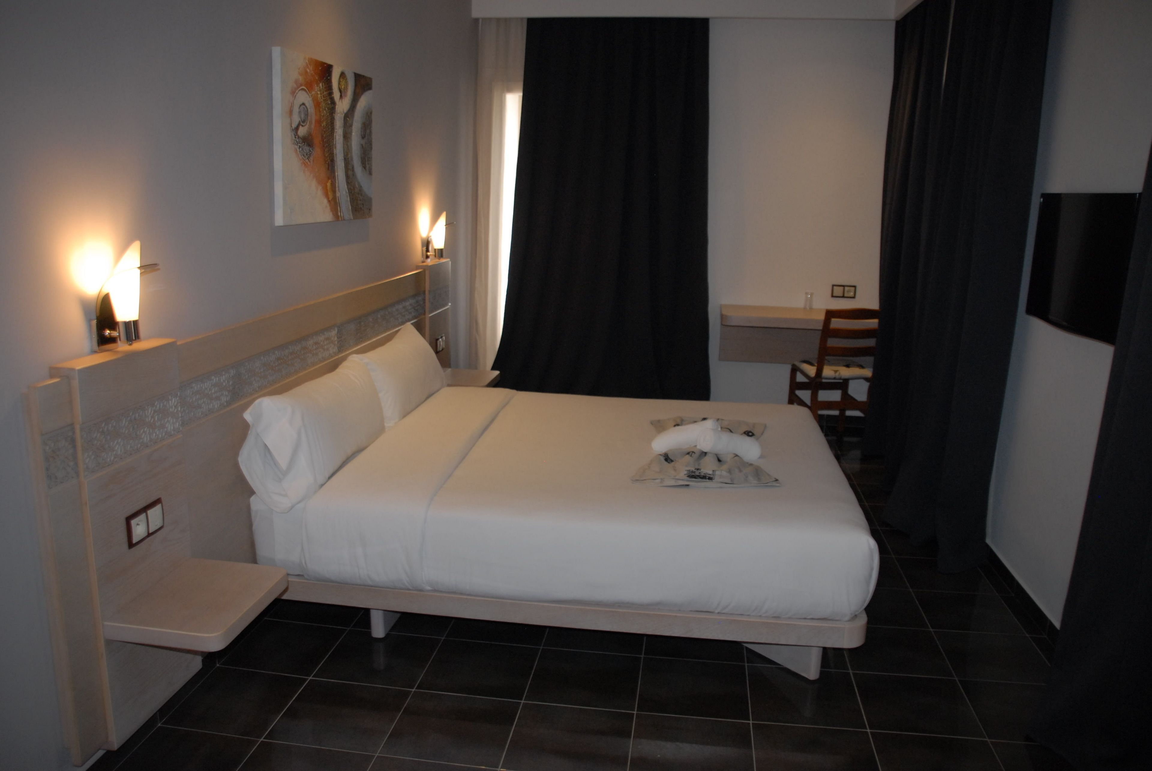 A hotel room with a large bed, bedside tables, a desk, and a chair.