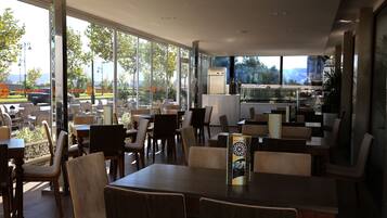 An indoor dining area with large windows, wooden tables, and chairs.