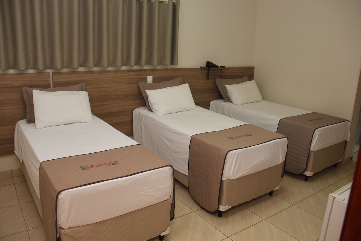 Ein Hotelzimmer mit drei Einzelbetten, jeweils mit brauner Bettdecke und weißen Kissen.